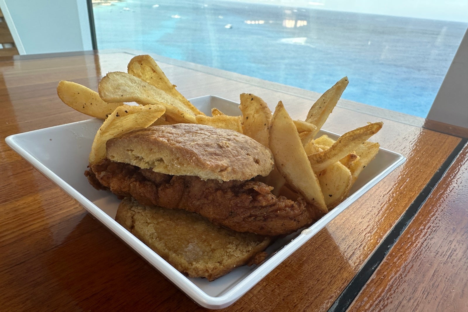 A white plate with fried chicken on a biscuit and French fries