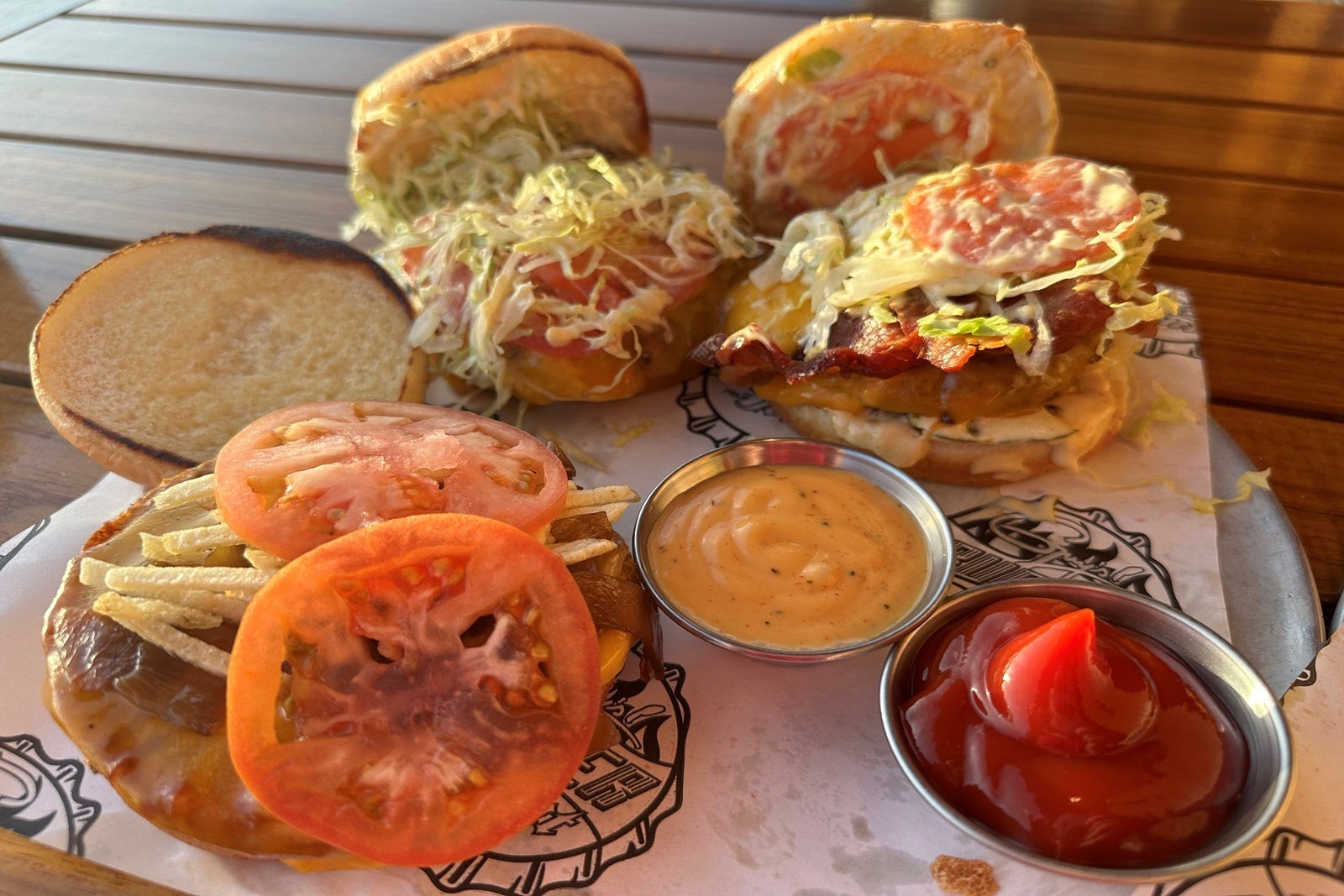Three burgers and dipping sauces on a plate on a wooden tabletop