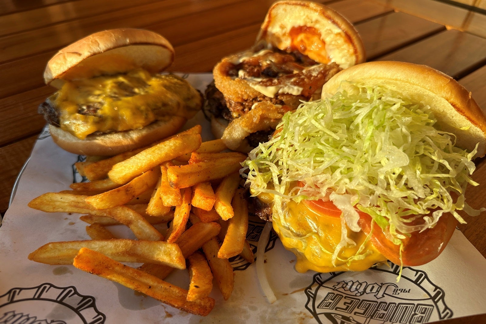 Three burgers and fries on a plate on a wooden tabletop