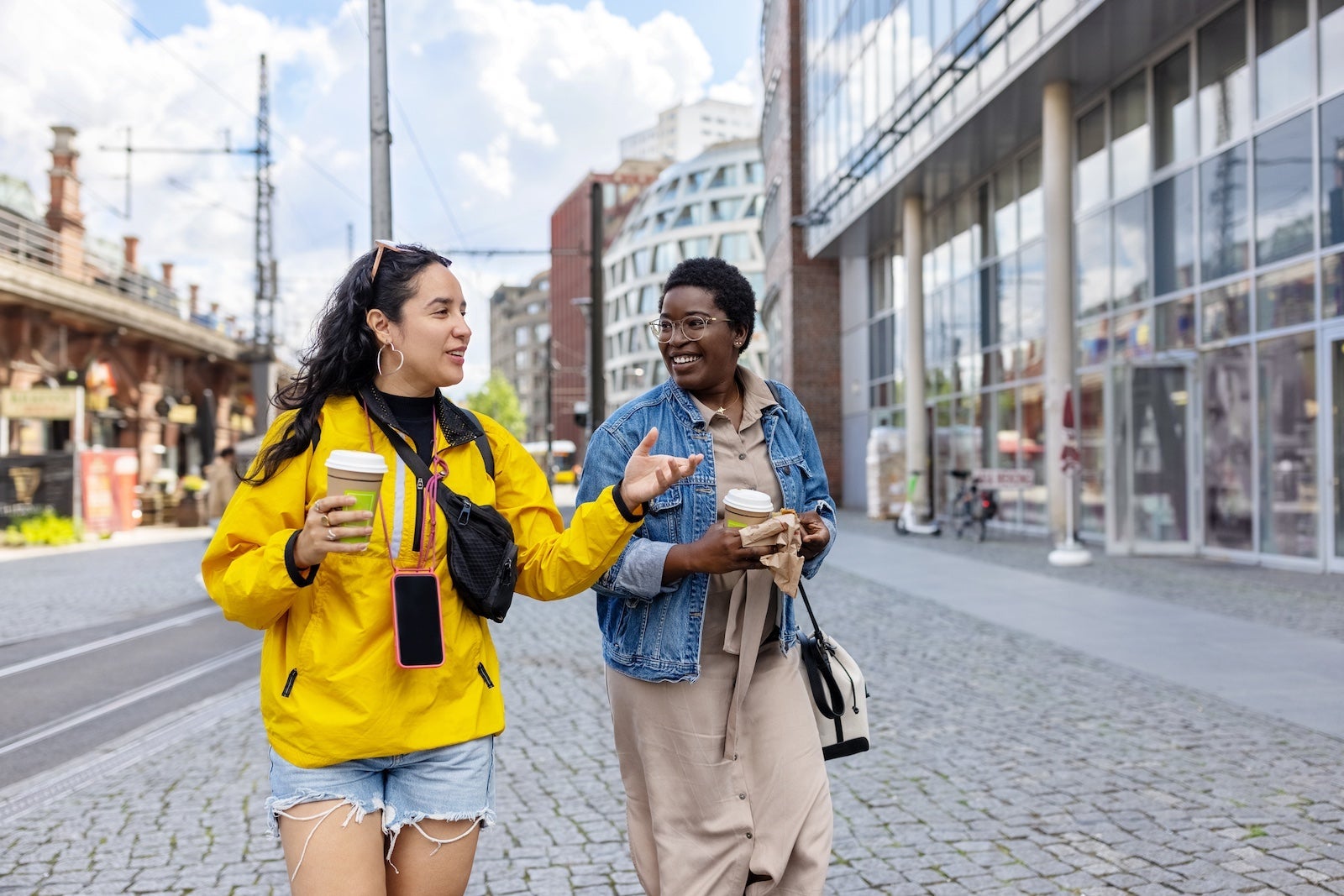Two female friends walking outside in the city. Diverse women holding coffee cups talking while walking outside in the city.