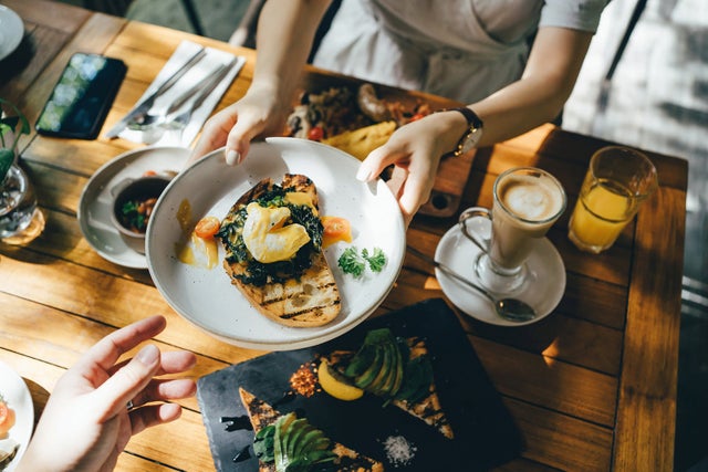 High angle view of woman passing platter of food to friend during brunch in an outdoor restaurant against beautiful sunlight