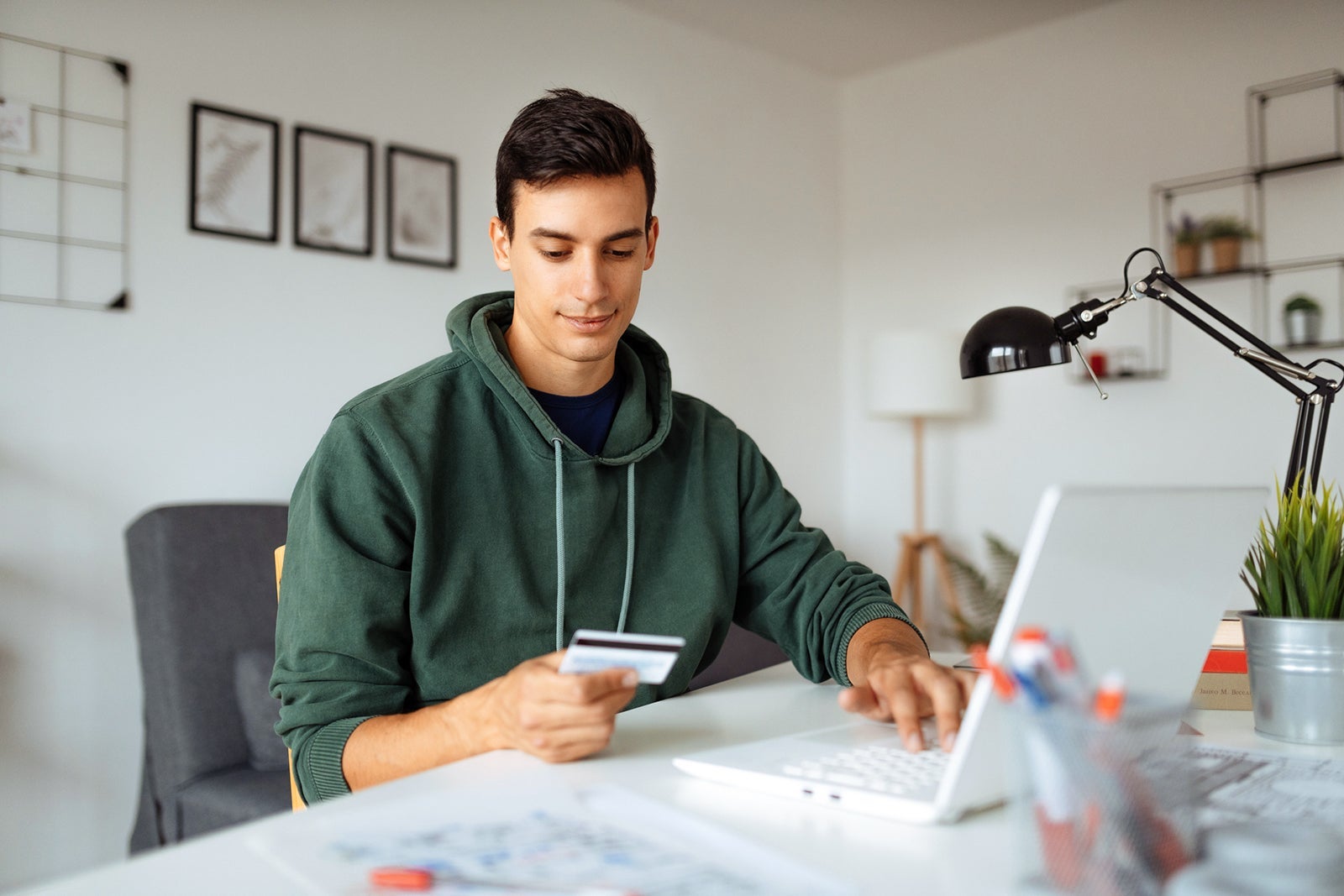 Young man looking at a credit card while using a laptop
