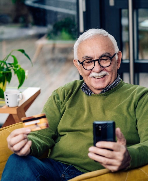 elderly man sitting in a chair holding a credit card and phone