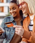 Two female friends using credit card and smart phone outdoors