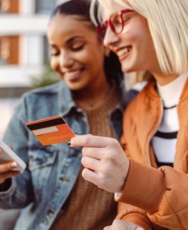 Two female friends using credit card and smart phone outdoors