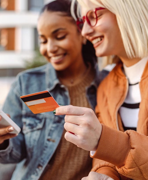 Two female friends using credit card and smart phone outdoors