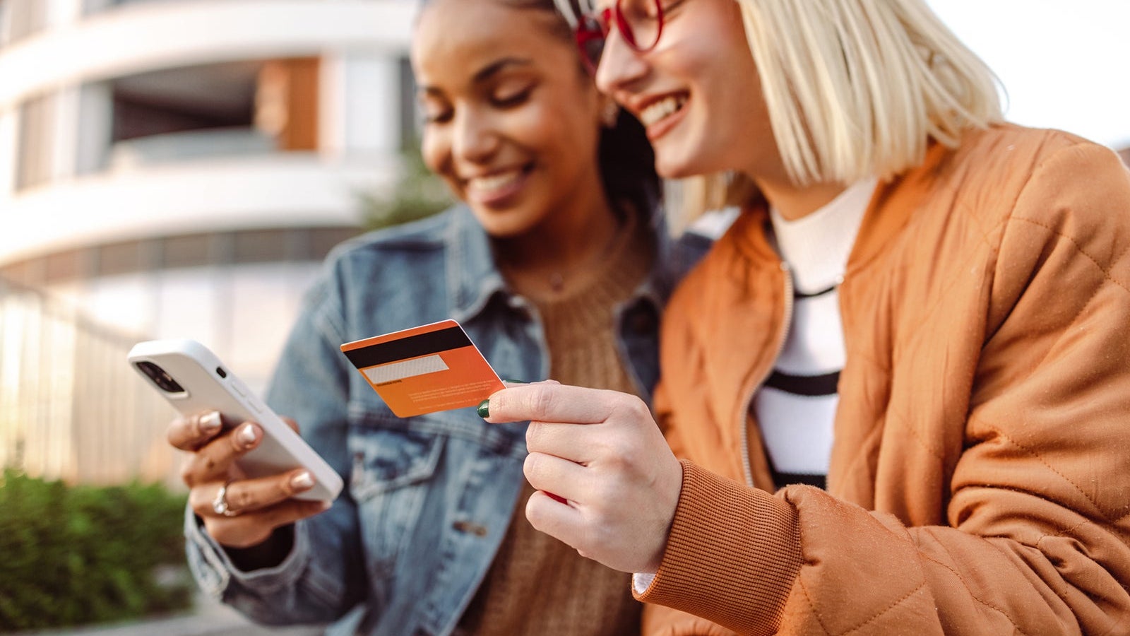 Two female friends using credit card and smart phone outdoors