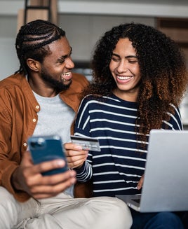 Young couple online shopping using mobile phone and laptop at home