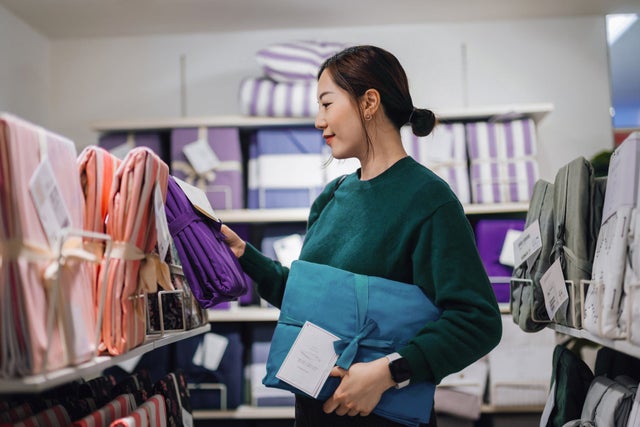 Young Asian woman shopping for home decor and household necessities in a homeware store, looking at bedding sets on a shelf