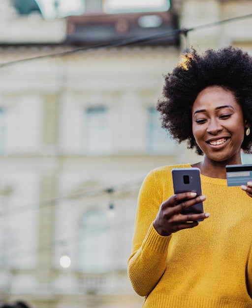 Woman outside holding credit card and looking at her phone