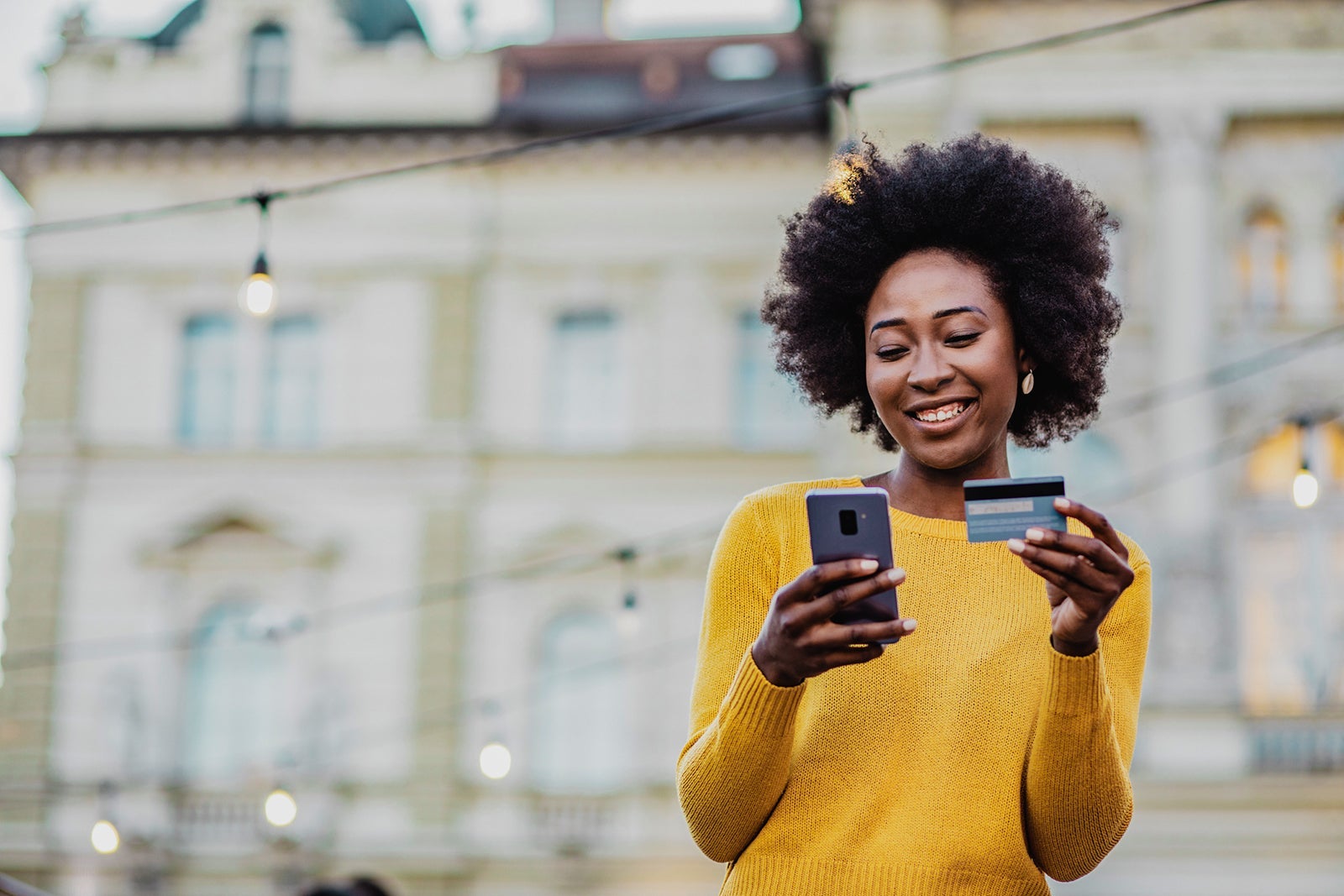 Woman outside holding credit card and looking at her phone