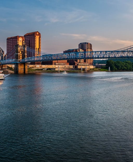 Paddle boat cruising the Ohio River as it passes under old suspension bridge between Cincinnati, Ohio and Covington, Kentucky.