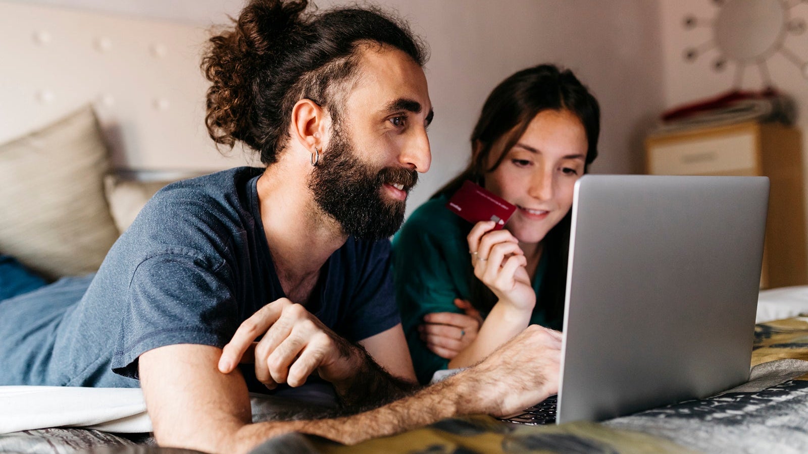 Happy couple lying on bed shopping online