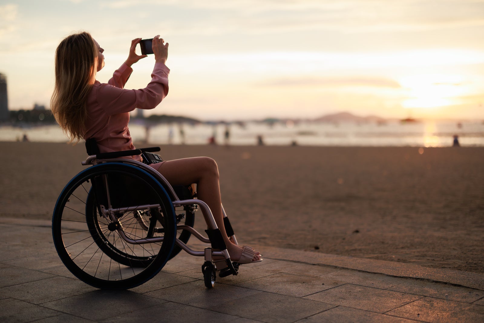 Woman in wheelchair takes photo beachfront. Pattaya, Thailand
