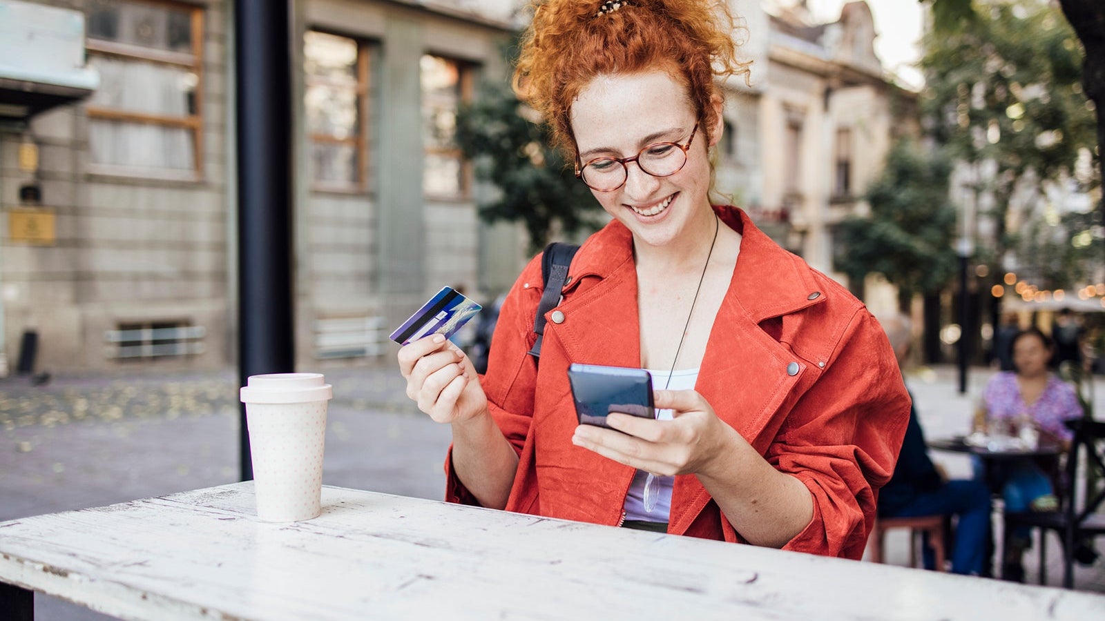 Portrait of a happy redhead girl enjoying coffee and shopping online at the cafe