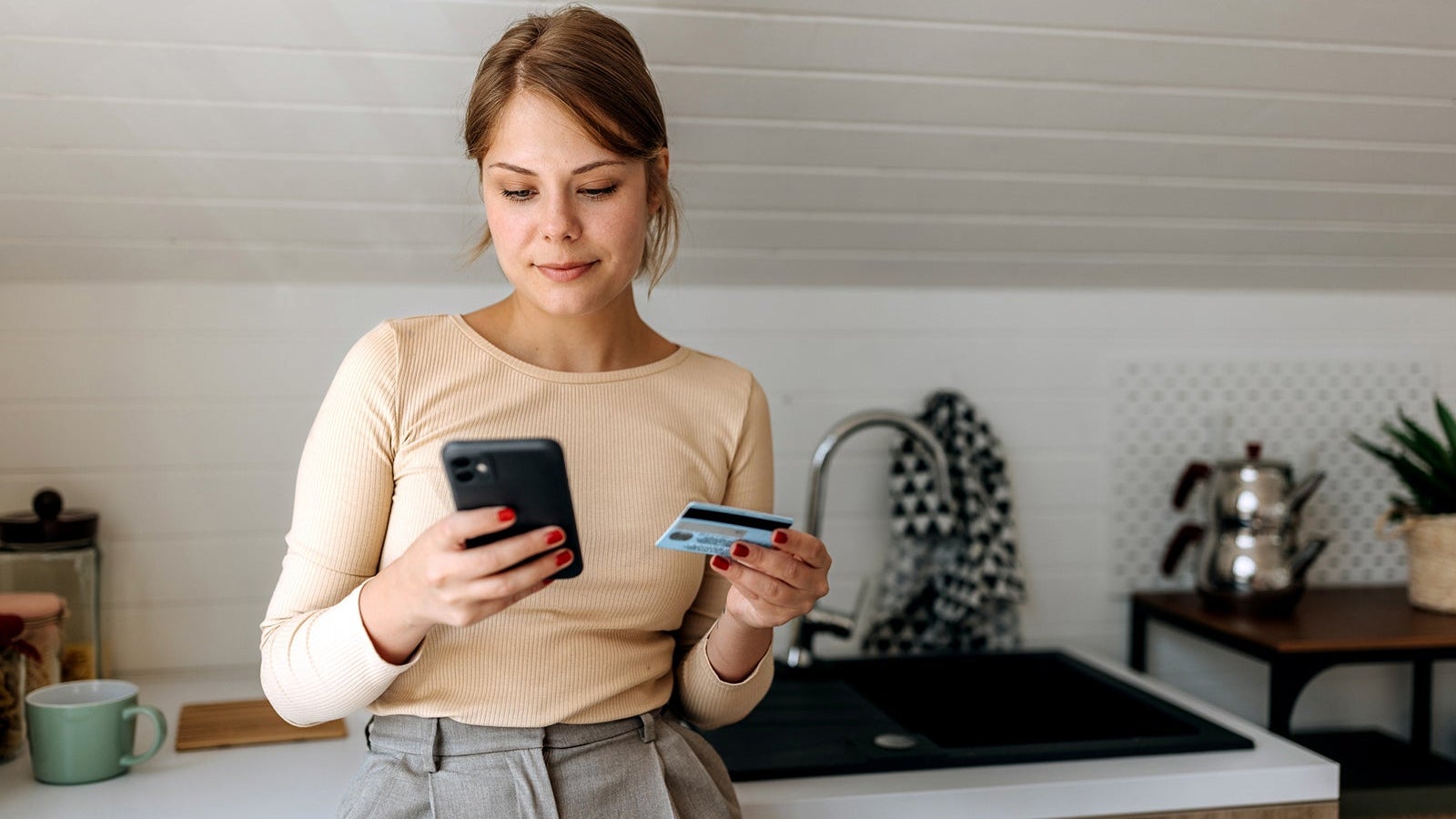 Young casually clothed woman online shopping from her domestic kitchen