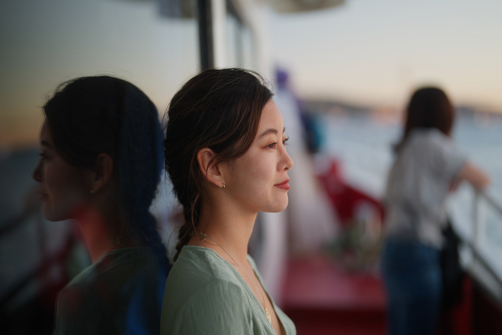 A woman stands against a window on the outer deck of a cruise ship looking longingly at the water