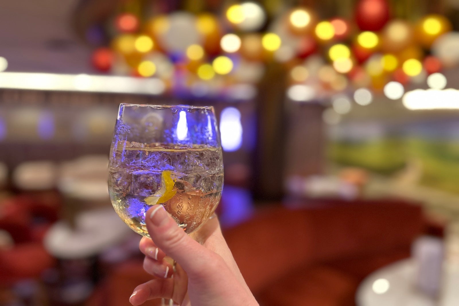 A hand holding a wine glass with lights blurred in the background