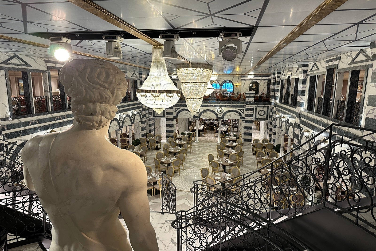A view of a cruise ship main dining room with a statue in front of the camera