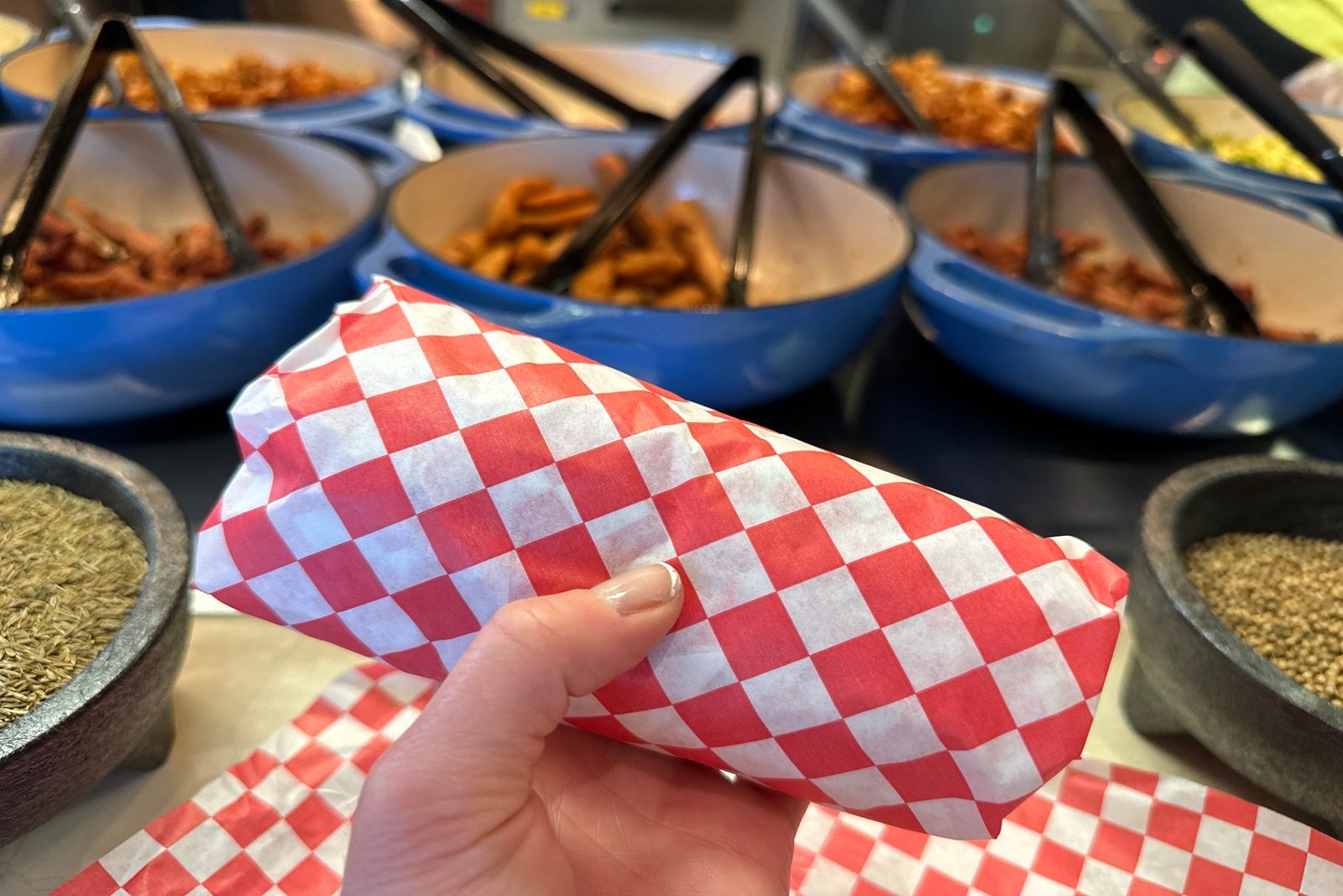 A hand holding a burrito wrapped in red and white checkered paper