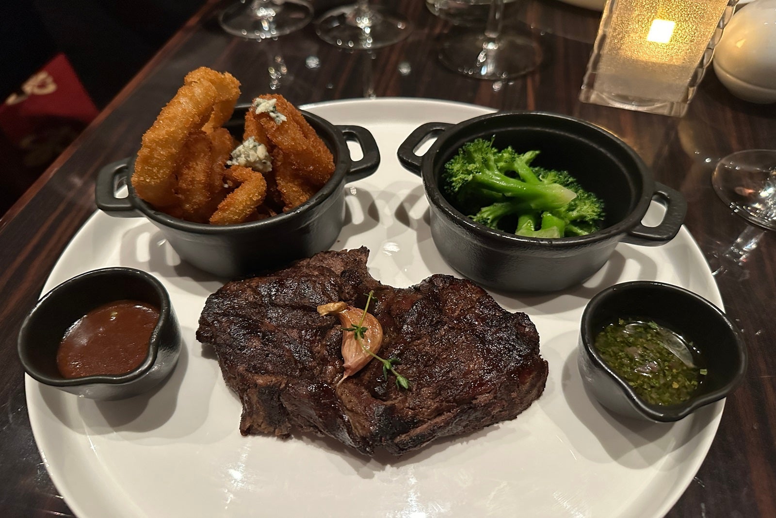 A plate with filet Mignon, onion rings, broccoli and sauce