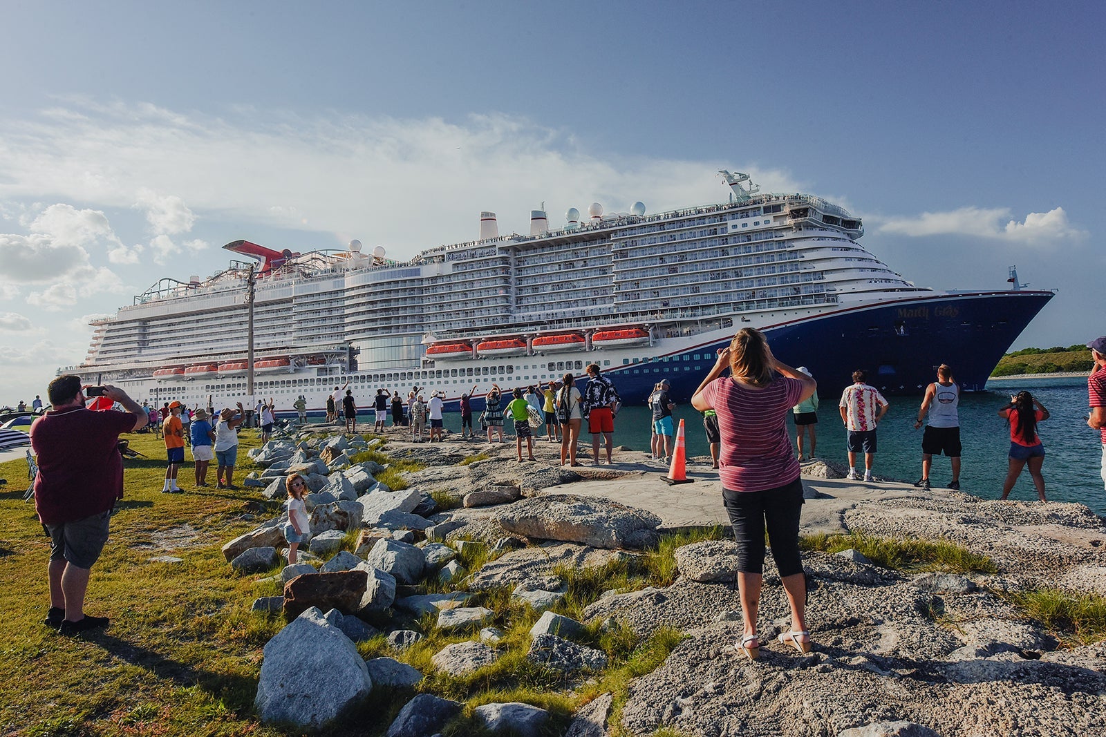 Locals standing on the shoreline looking at a large cruise ship that's docked