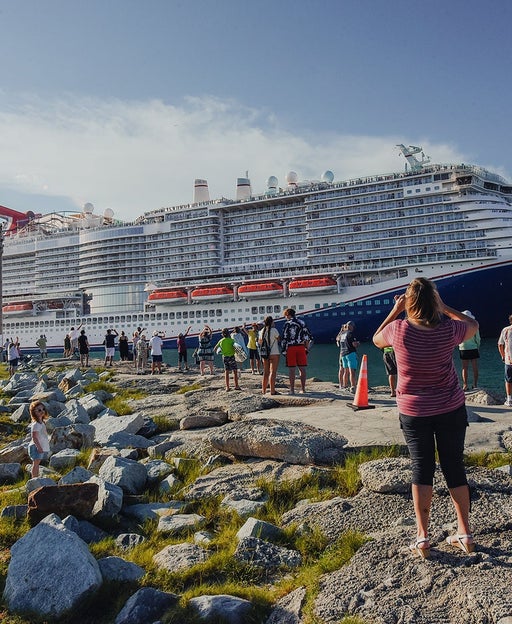 Locals standing on the shoreline looking at a large cruise ship that's docked