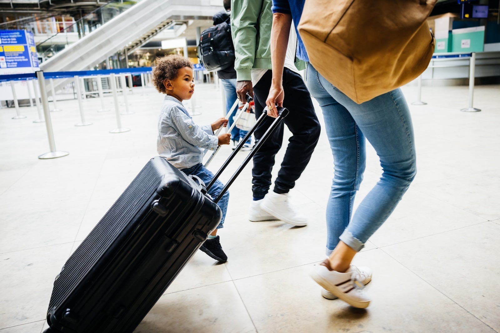 A child sitting on a suitcase while being wheeled through an airport