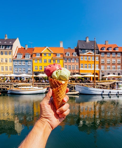 A person holding an ice cream cone in front of a canal and a row of houses