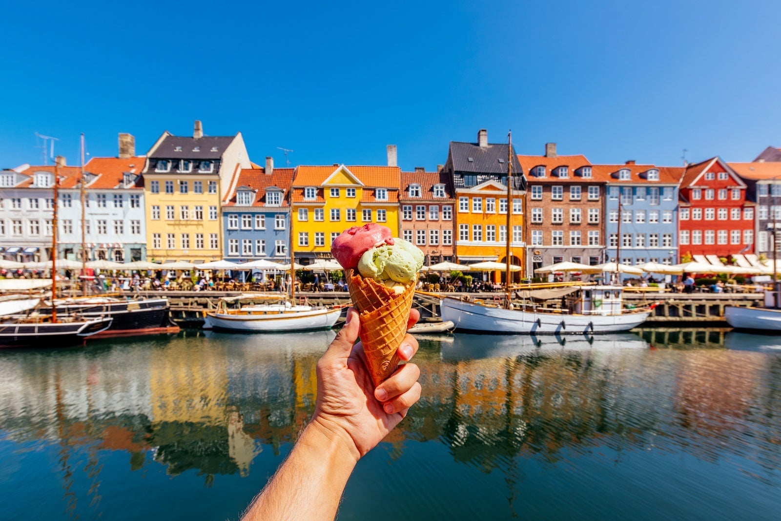 A person holding an ice cream cone in front of a canal and a row of houses