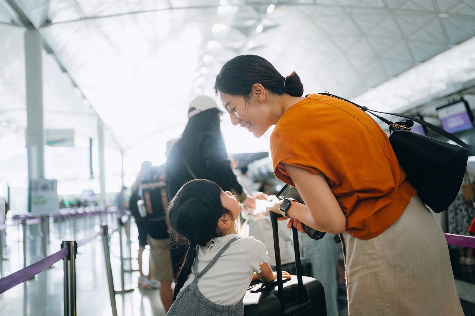 Joyful young Asian mother and little daughter travelling together, they are waiting in line for the check-in counter at airport terminal. Ready for a trip. Travel and vacation concept