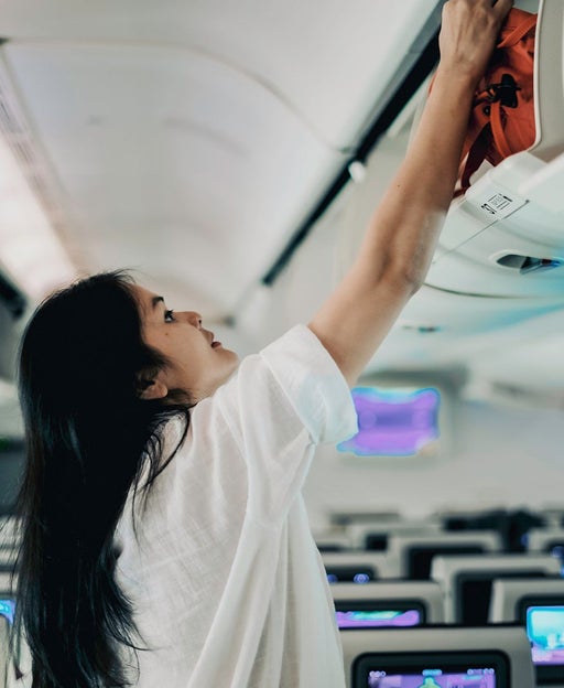 A woman putting away her bag in the overhead compartment