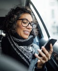 Mature businesswoman using phone while traveling by a taxi