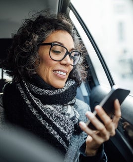 Mature businesswoman using phone while traveling by a taxi