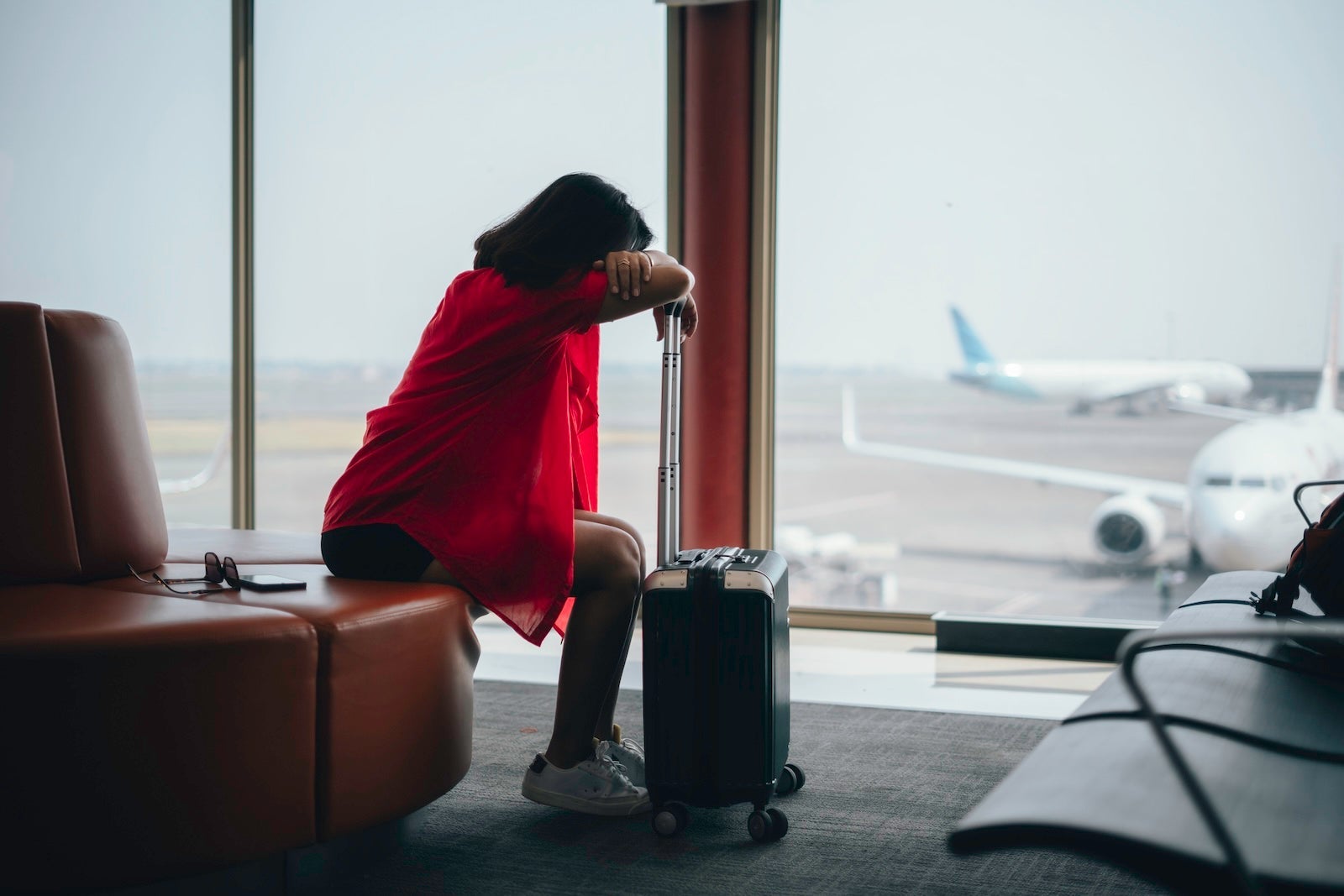 Woman hunched over carry on luggage, waiting at the airport