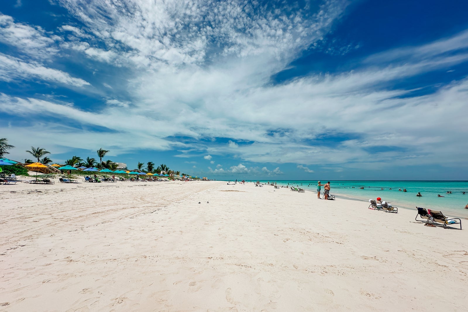 A deep stretch of beach with blue sky, ocean and umbrella loungers
