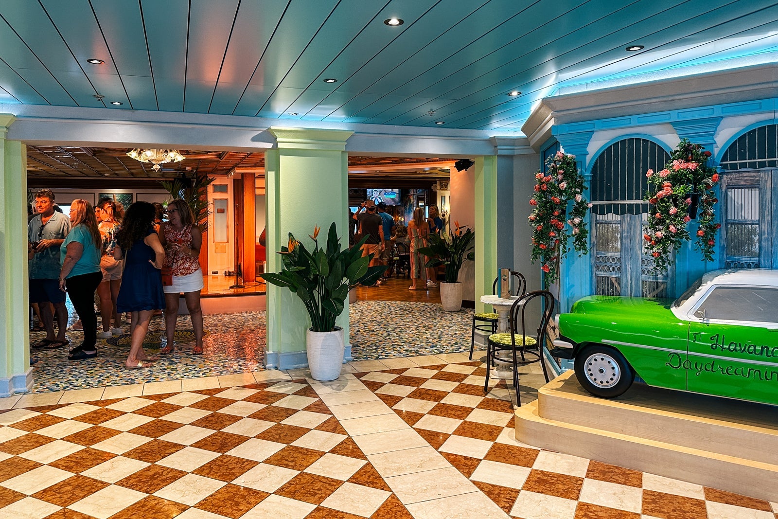 A cruise ship bar with a checkered dancefloor, an old-timey green car replica and an area for sitting