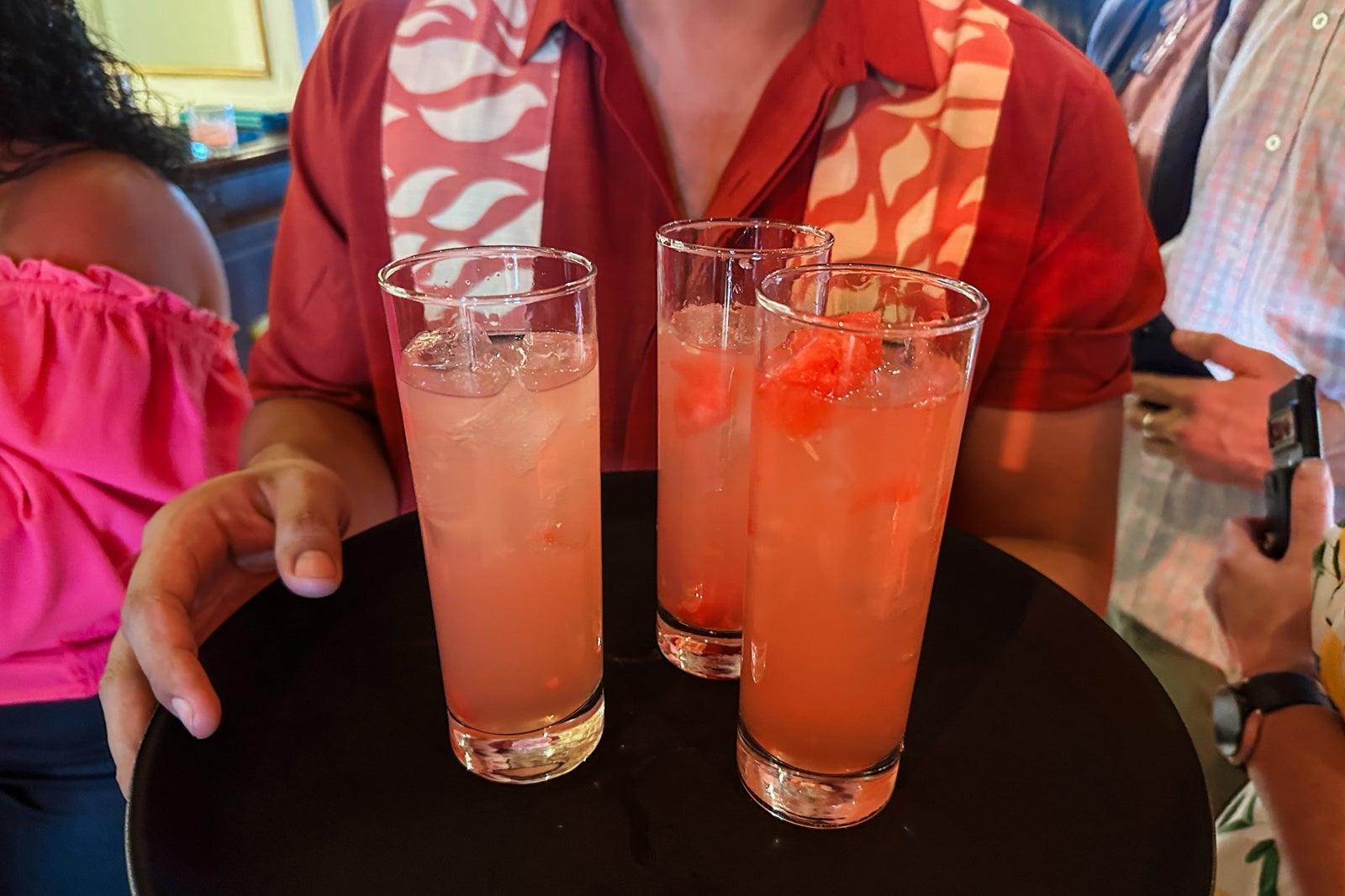 A cruise ship crew member holding a round black tray with strawberry drinks on it