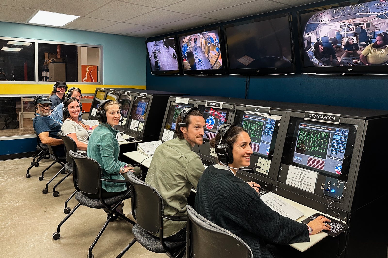 a group of adults sit at a series of computers at Space Camp during a Mission Control Exercise