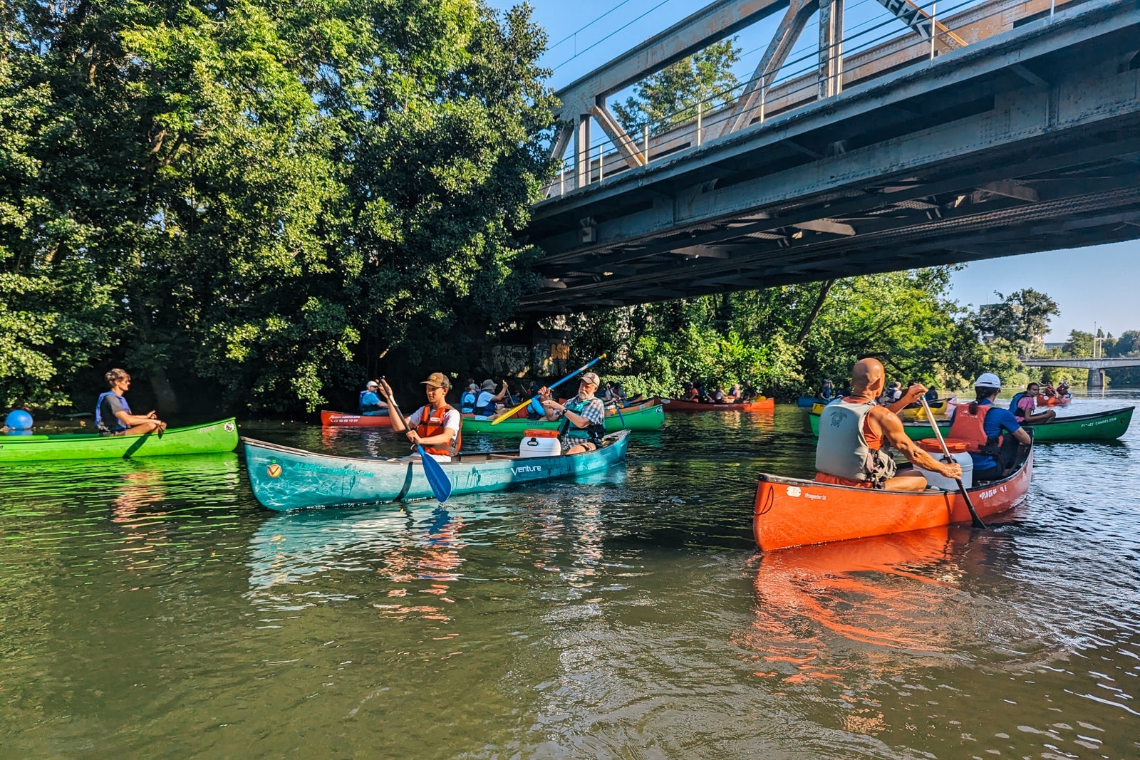 Brightly colored canoes paddling under a bridge