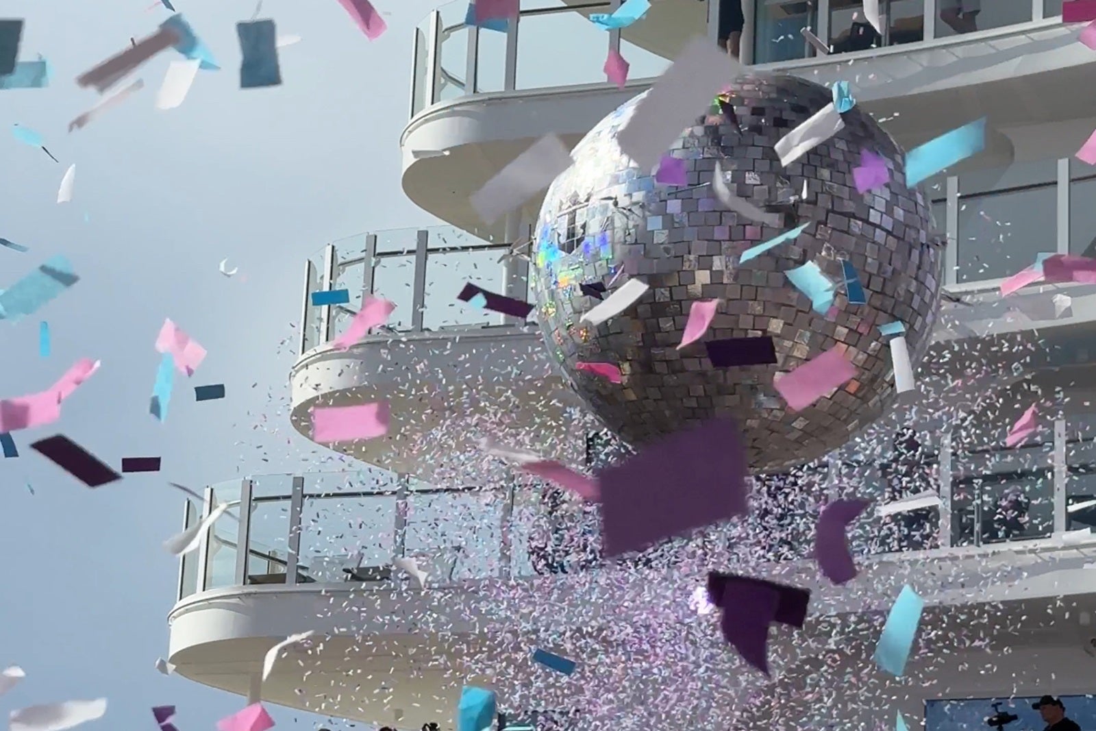 A disco ball with the Royal Caribbean logo with confetti in the foreground and aft cruise ship decks in the background