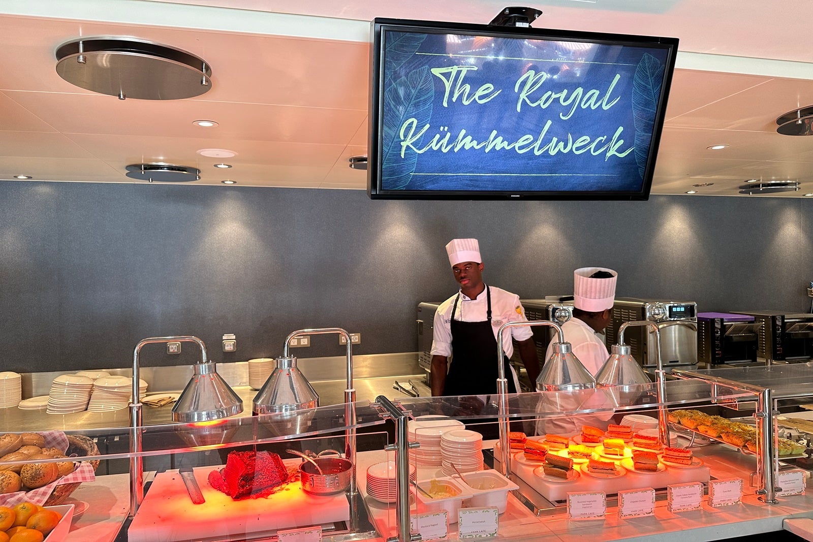 A deli service counter with two chefs and a TV sign that says "The Royal Kummelweck"