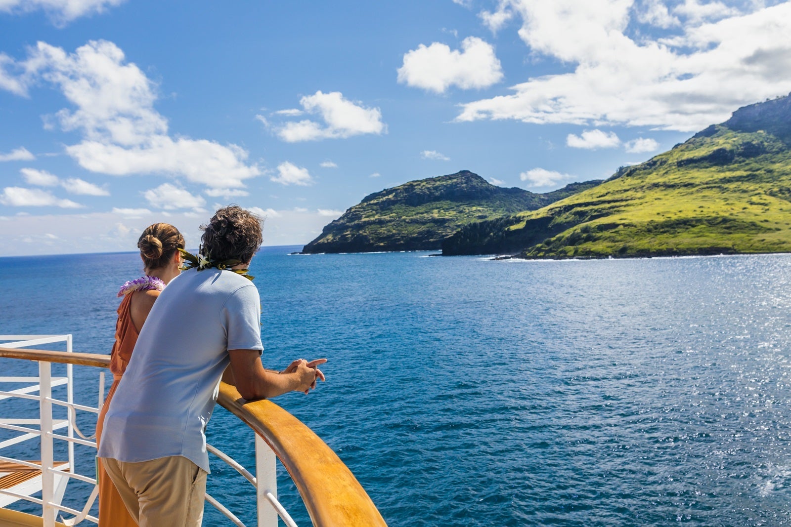 A couple standing along the railing of a cruise ship looking at the greenery of the Hawaiiain islands