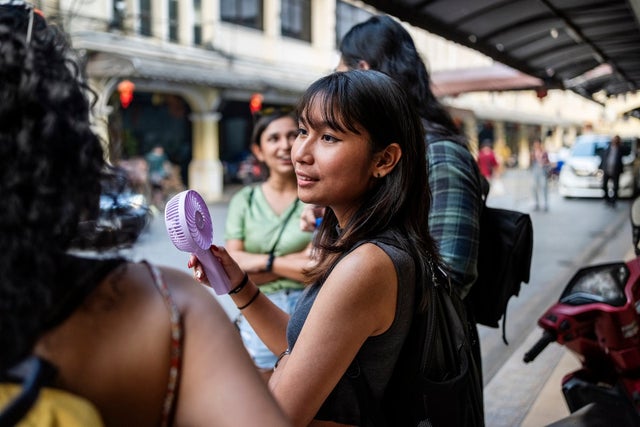 Asian woman using a portable fan in hand sightseeing with group of friends in foreign city on hot summer day