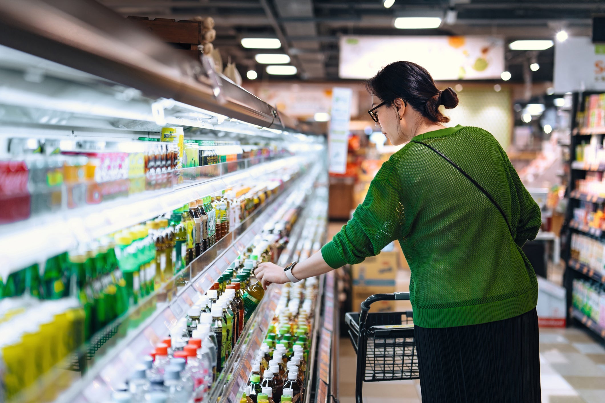 Young Asian woman with shopping cart picking up a bottled drink