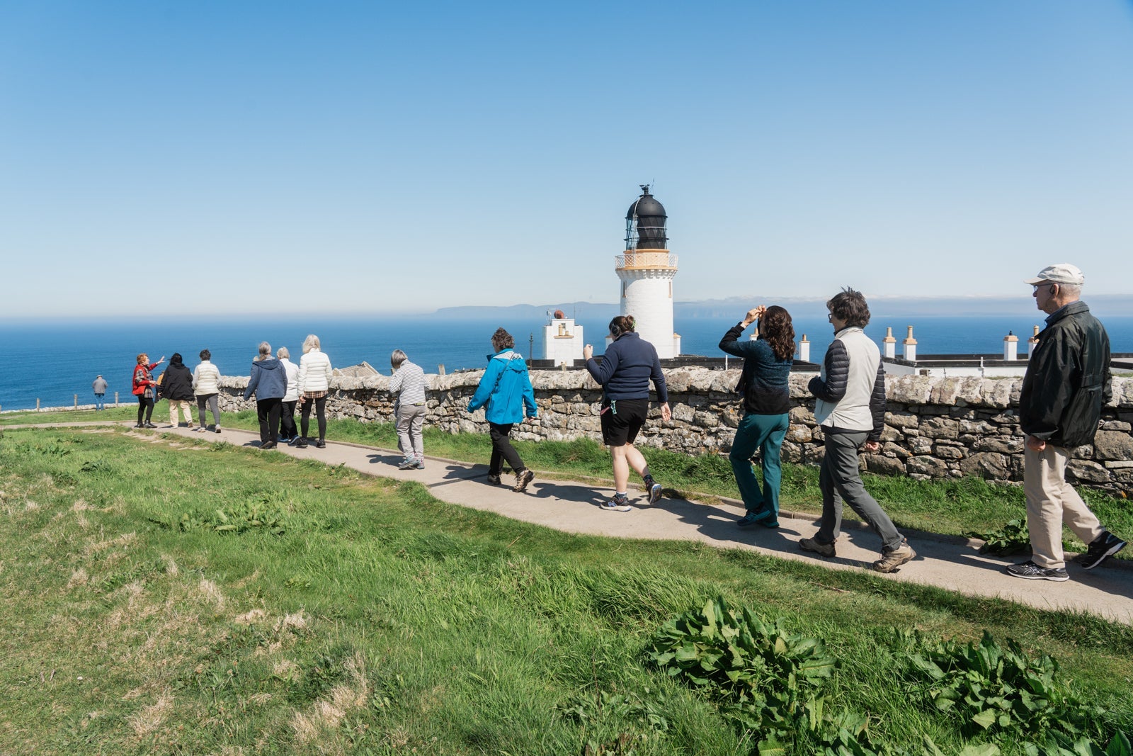 Tourists walk by Dunnett Head Lighthouse, Scotland.