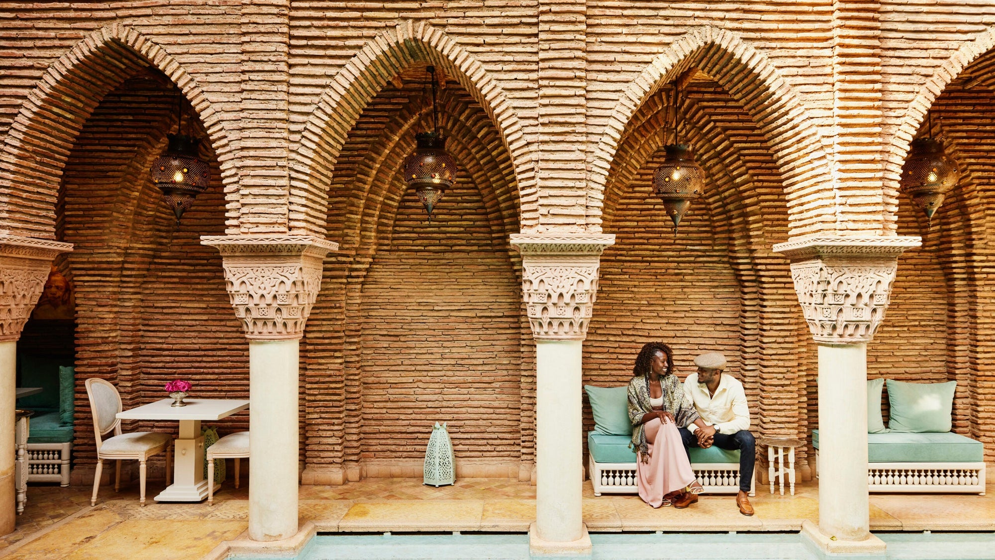 Wide shot of couple holding hands while sitting in courtyard of luxury hotel