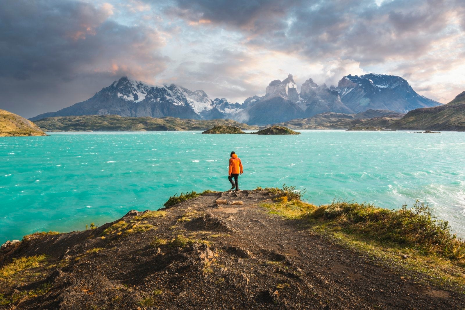 man hiking in front of blue lake and mountains in Chile