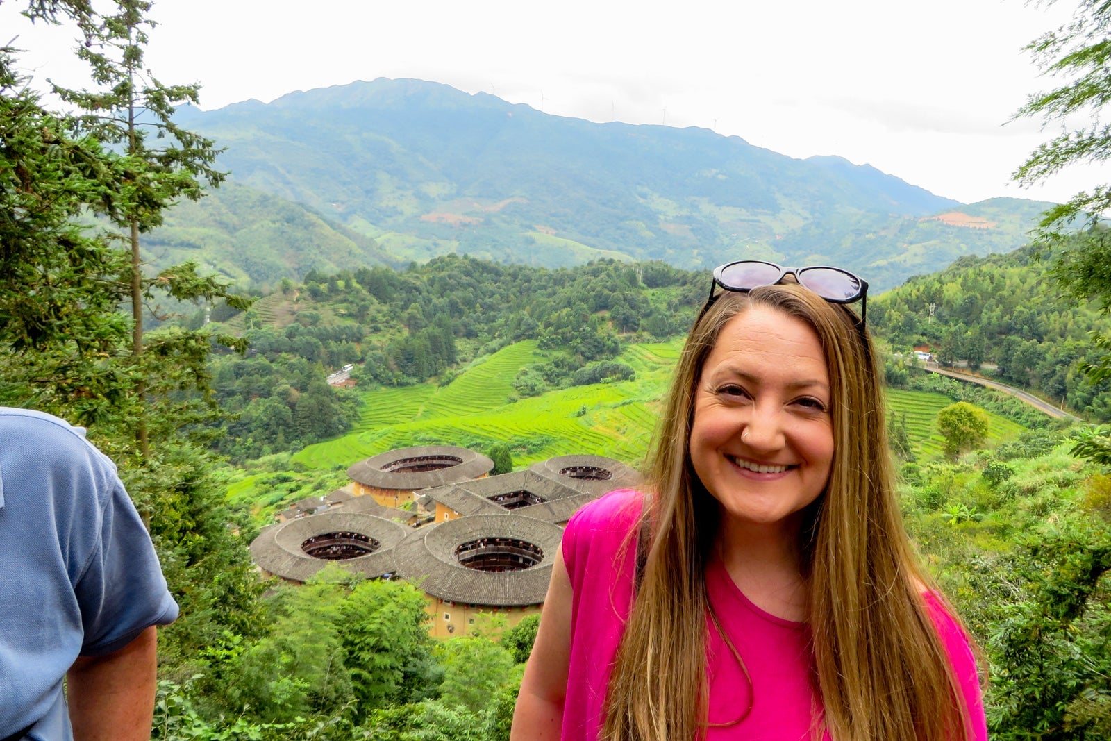 A woman in a pink shirt with round Chinese buildings in the background