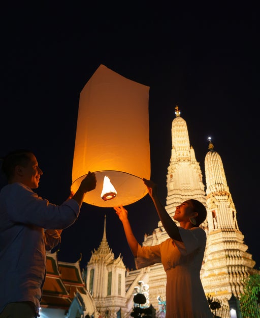 Mixed race romantic lover couple in Wat arun in night time and floating lamp in Yi Peng festival under Loy Krathong day, Bangkok city ,Thailand